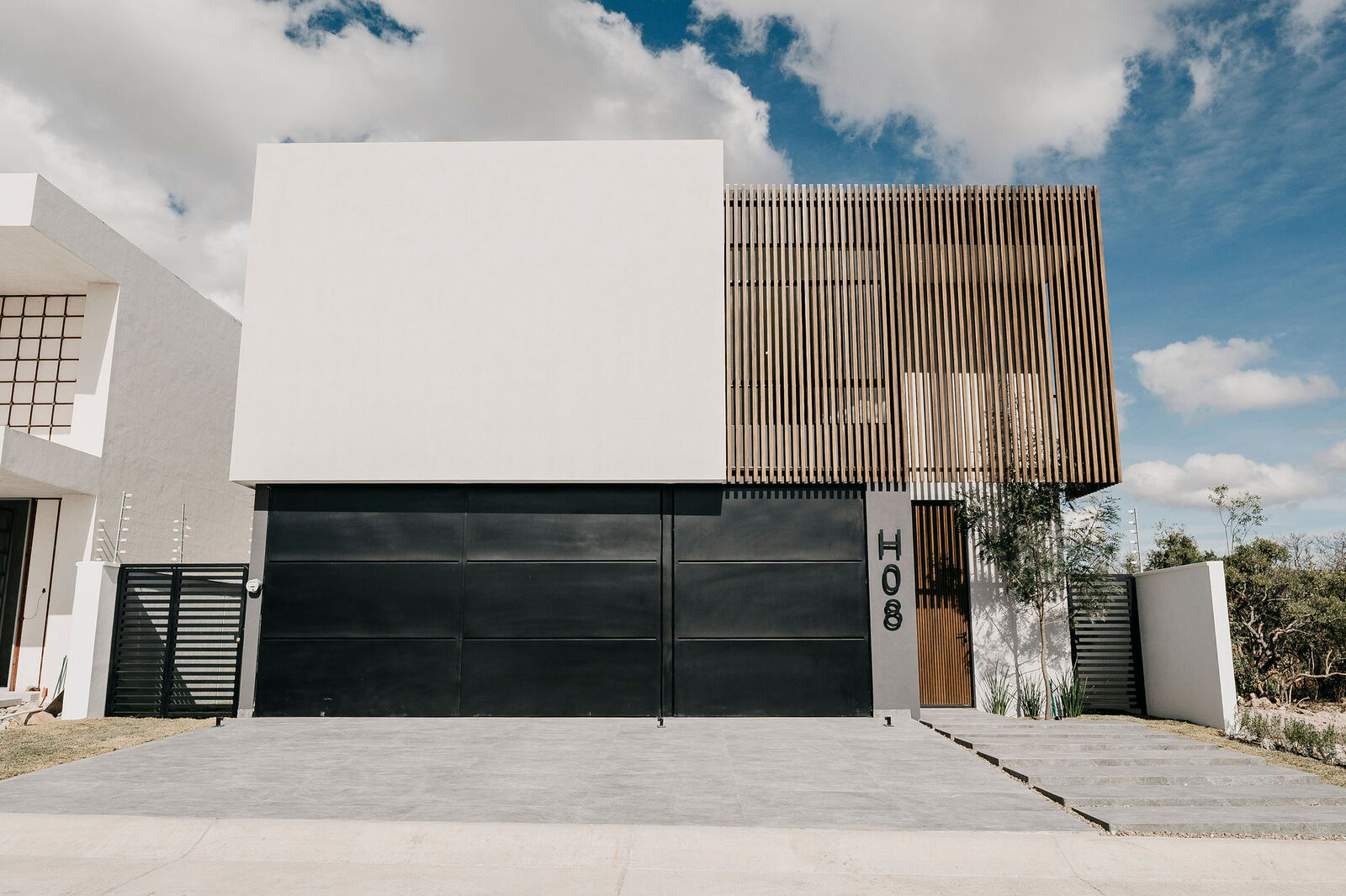 Fachada blanca con portón oscuro y celosía de madera